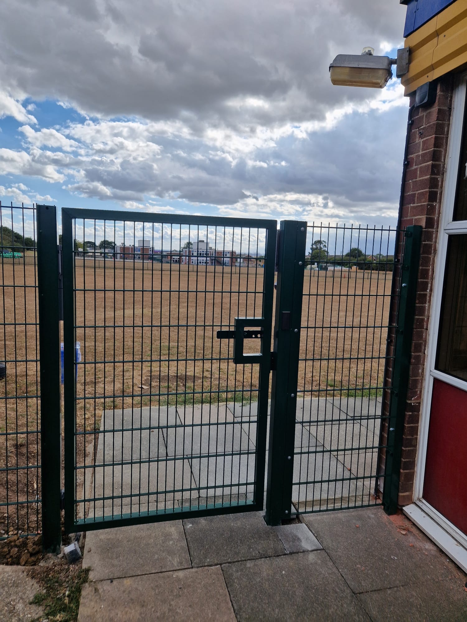 Green mesh pedestrian gate beside the school building looking across the field