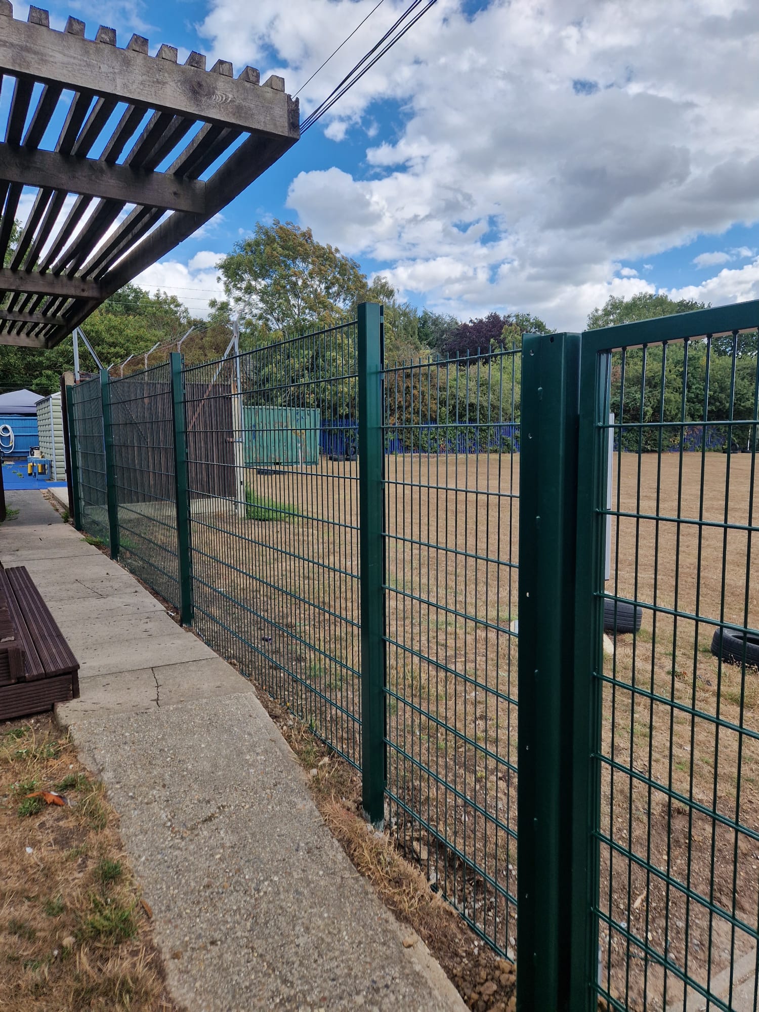 Green twin-wire mesh fencing running past the school pergola and playing field