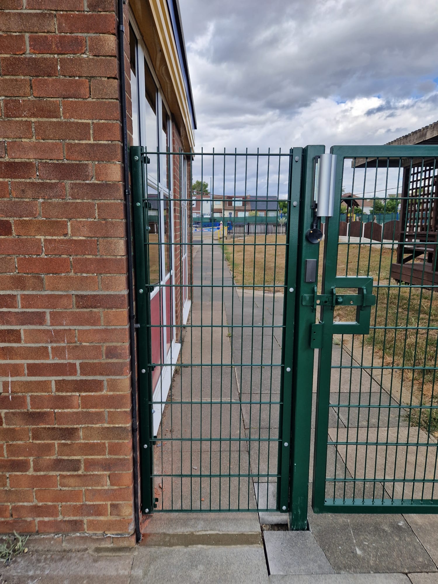 Green steel mesh security gate controlling access beside a commercial building