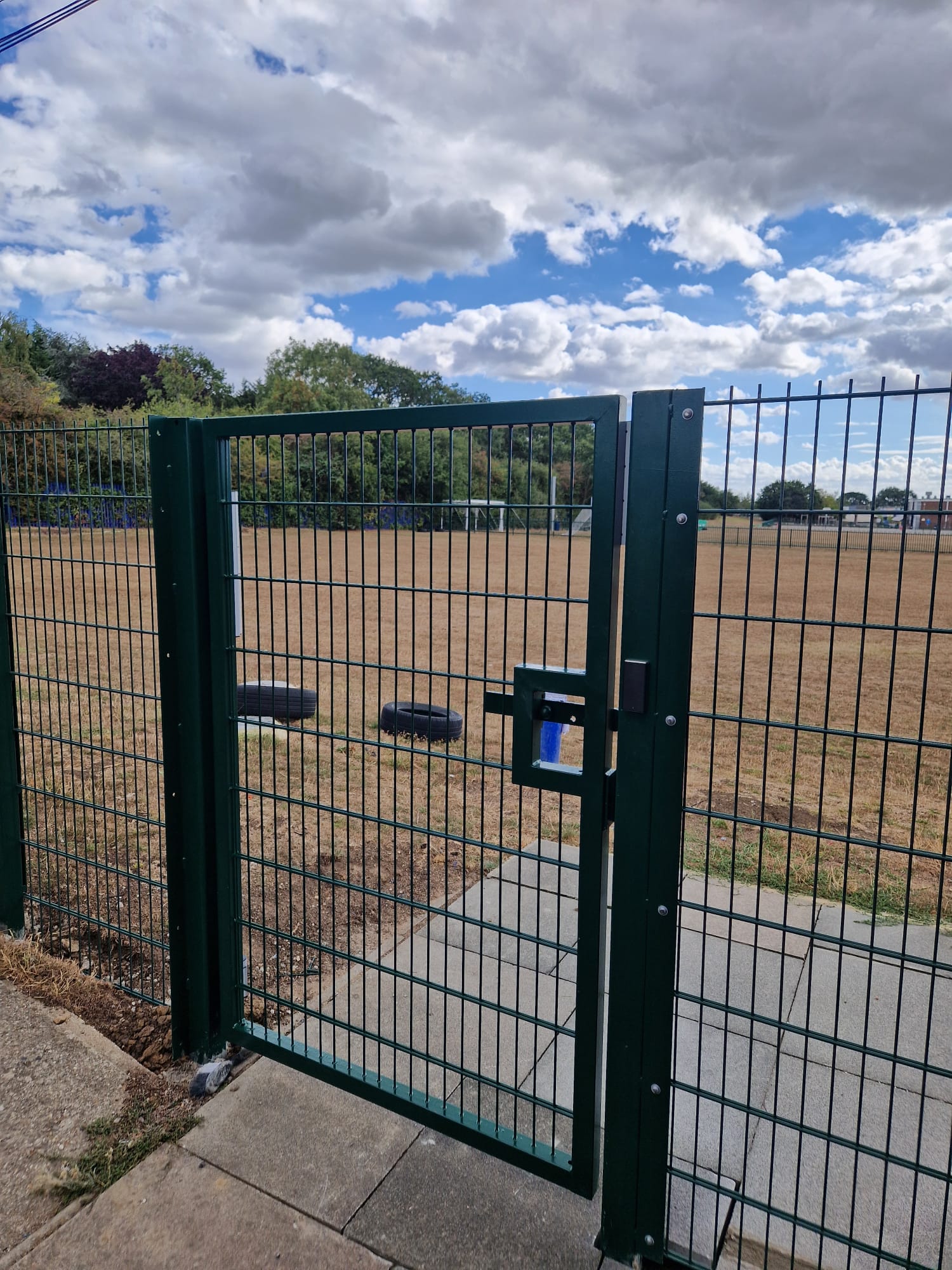 Green mesh gate opening onto a playing field