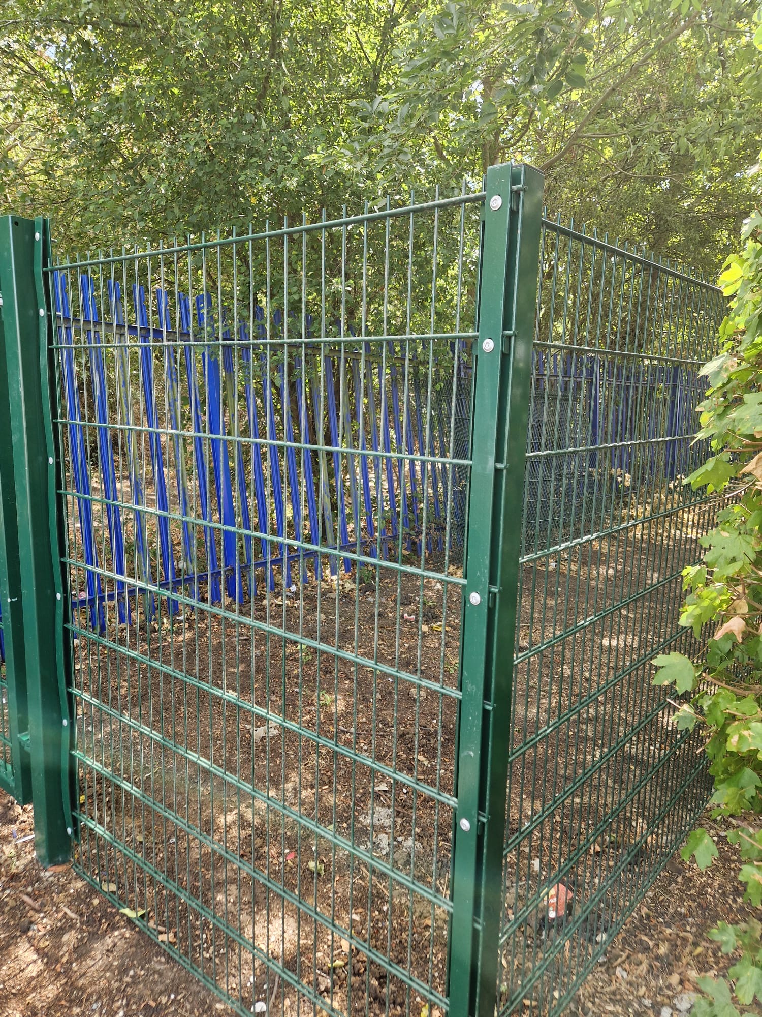 Green twin-wire mesh fencing enclosing a boundary in a wooded setting