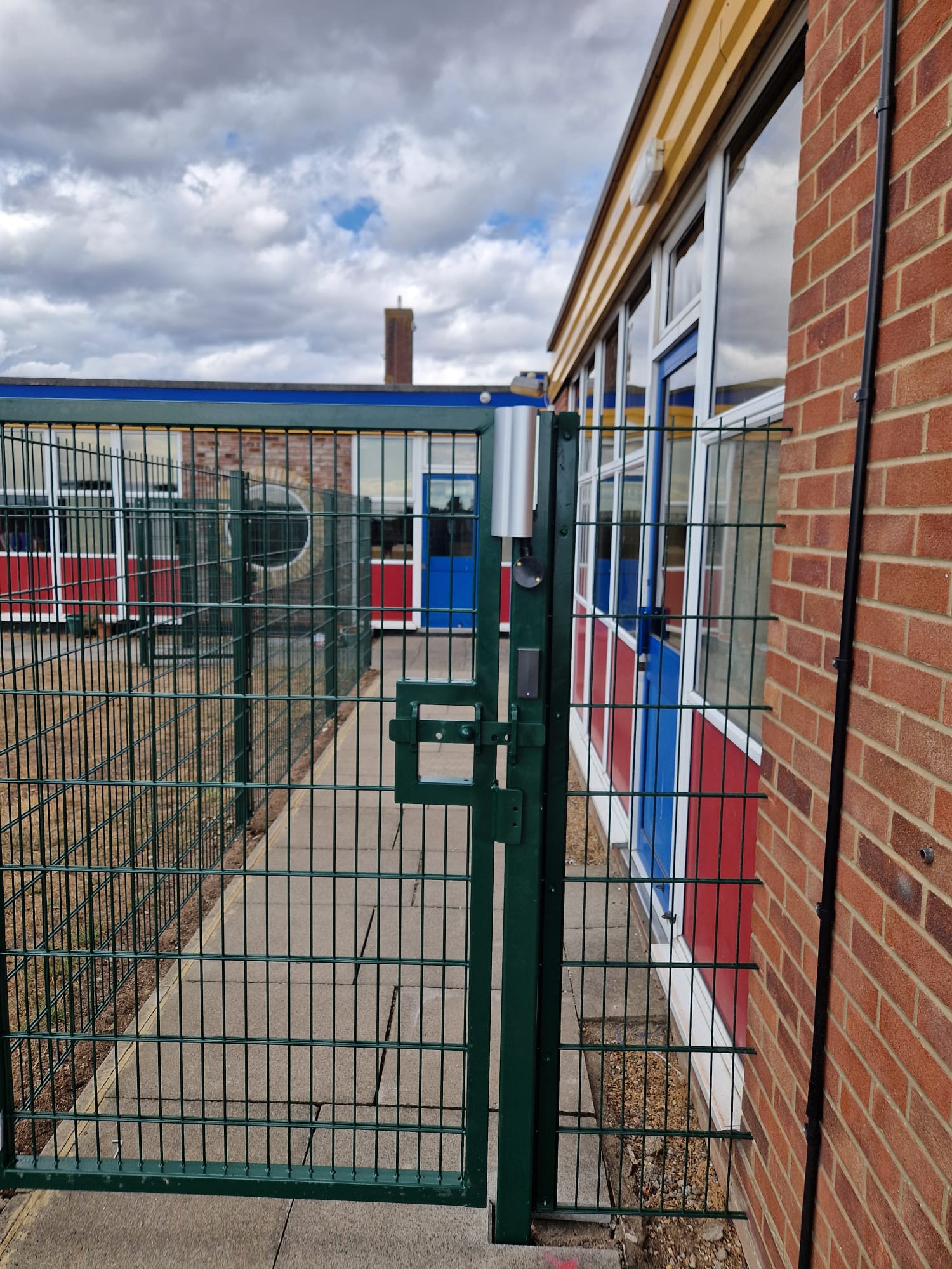 Green mesh gate with hydraulic closer and card reader between school buildings